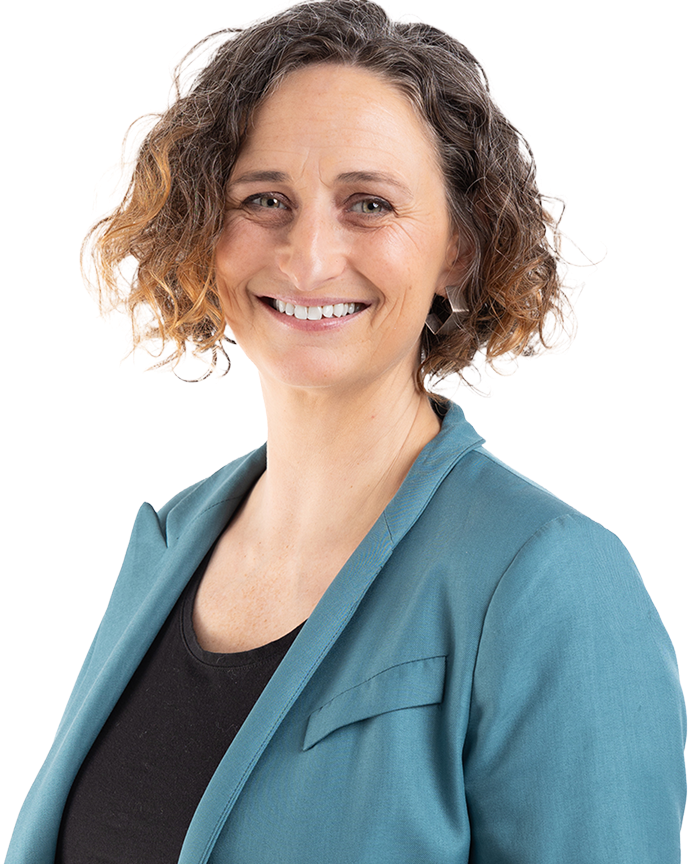 Professional headshot of Lynn Boylan with curly hair, wearing a teal blazer over a black top, set against a neutral indoor background.